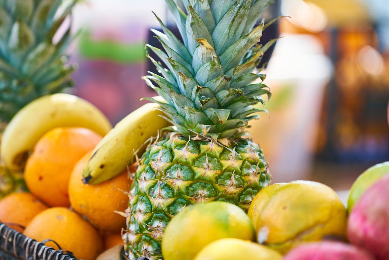 Close-up of a colorful fruit basket featuring a ripe pineapple, bananas, and oranges.